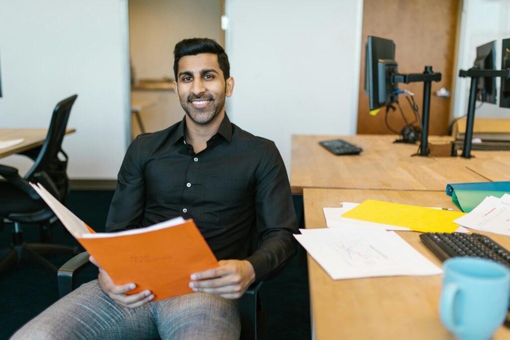 Smiling businessman holding documents at his desk, embracing productivity in a modern office.